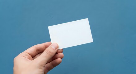 Obraz premium Hand holding blank white business card against blue background for mockup and branding design projects.