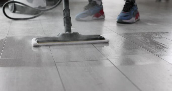 Steam mop head glides cleaning dirty floor tiles. Hot device sanitizes laminate surface removing stains from spacious modern kitchen area apartment