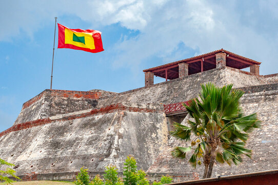 The massive stone walls of San Felipe de Barajas Castle rise above green lawns and palm trees under a cloudy sky in the coastal city of Cartagena, Bol&iacute;var, Colombia