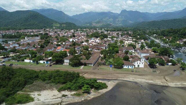 Circling drone view of Paraty, with the beach, the mountains and the Atlantic forest that surrounds this historic city