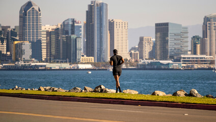 A physically fit man dressed in black jogging on a trail with the City of San Diego in the background © F Armstrong Photo