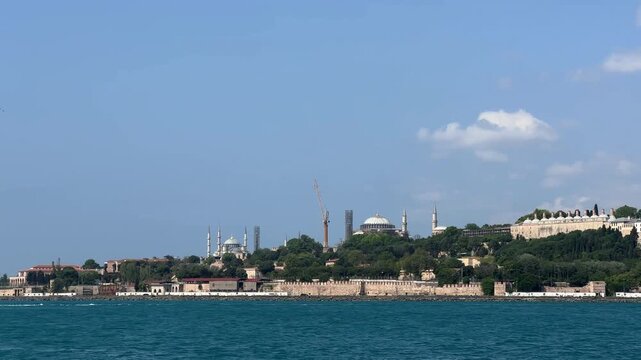 Scenic view from the water of Topkapi Palace courtyard, Blue Mosque, and Hagia Sophia rising above Istanbul&rsquo;s historic skyline, blending Ottoman and Byzantine architecture under clear skies.