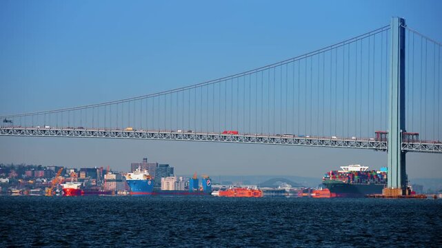 New York, USA, 24 December 2025: Verrazzano Bridge with container ships. Container vessels pass beneath Verrazzano Narrows Bridge in New York Harbor.