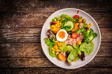 Tuna salad with tomatoes, cucumber, corn, olives , eggs and onion on wooden background, top view. High quality photo