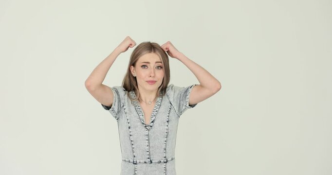 Young woman in denim dress lifts both fists above head. Person hits head lightly in regret while showing comic frustration about silly mistake