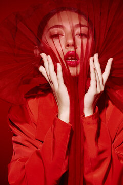 Creative beauty portrait of a woman in bright red fashion attire and veil showing open lips and life detail close-up. Concept of bold style, glamour, and artistic expression.