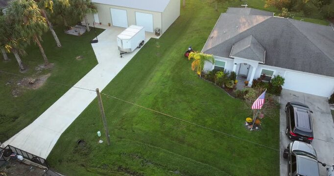 Man riding zero turn lawn mower cutting grass in summer at Florida house yard.