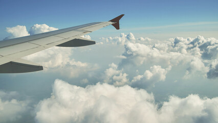 Obraz premium Airplane wing flying above the clouds on a sunny day