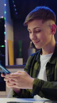 Teenager boy sitting at table holding smartphone enjoying using mobile apps, playing games texting SMS message learning online. Male working remote with technology. Slow motion.