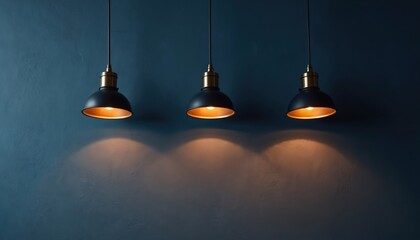 Obraz premium Three dark pendant lamps with gold interiors hang against a textured dark blue wall. Warm light spills downwards creating soft illuminated circles on the rough surface.