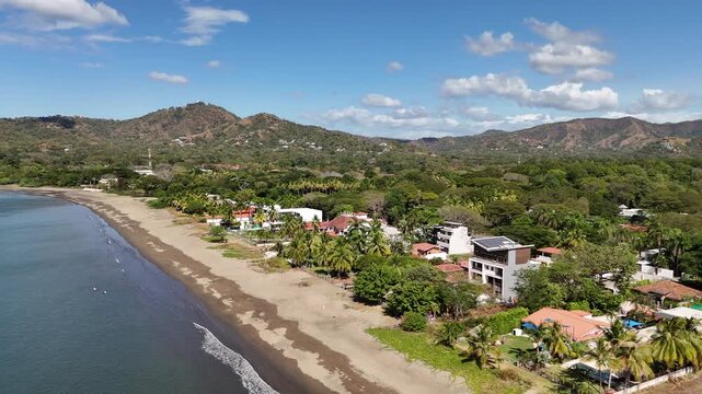 Aerial beachfront villas surrounded by palm trees overlooking small waves breaking on sandy beach in Guanacaste Costa Rica.
