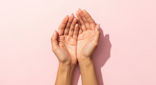 Two hands cupped together in a gesture of prayer or supplication against a soft pink background with shadow
