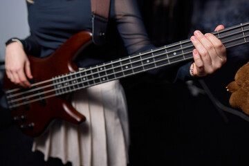 Obraz premium Female bassist rehearsing. Female musician with bass guitar. Female performer practicing in dim studio lighting. Female bassist preparing for performance in moody rehearsal space