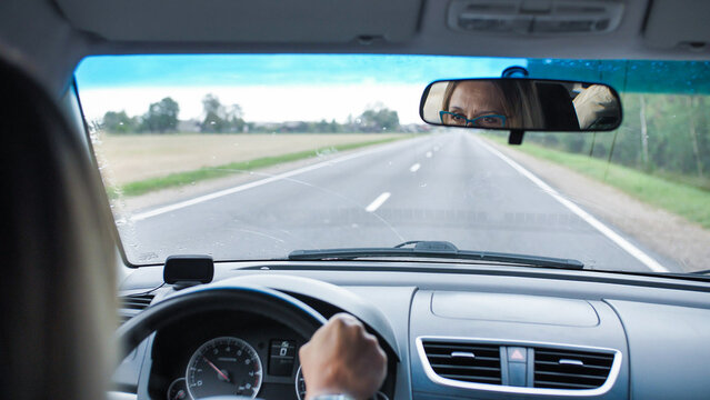 Woman driving car on open road, looking in rearview mirror, traveling concept