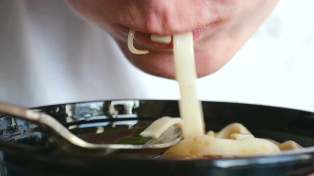 Close up person mouth while eating hot udon noodle soup with spoon from black bowl, enjoying delicious, savory asian meal for lunch or dinner with gusto. Person eating delicious hot asian noodle soup