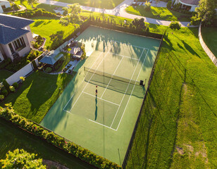 A stunning aerial shot captures a lone player on a private tennis court at golden hour. Long shadows and vibrant greens evoke themes of luxury, dedication, and an elite suburban lifestyle.