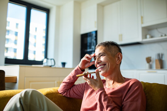 Smiling adult using voice assistant on smartphone at home