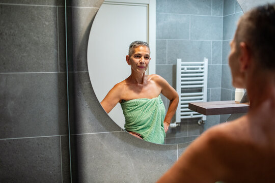 Confident mature woman in towel looking in bathroom mirror