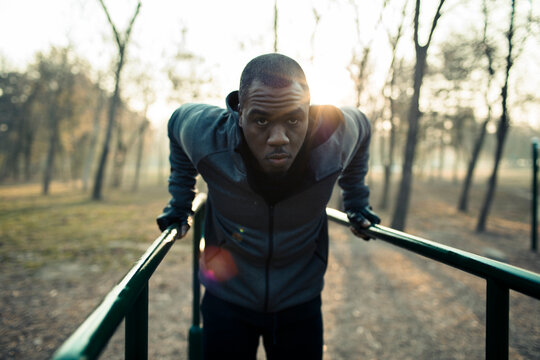 Man doing triceps dips on parallel bars in a park at sunrise