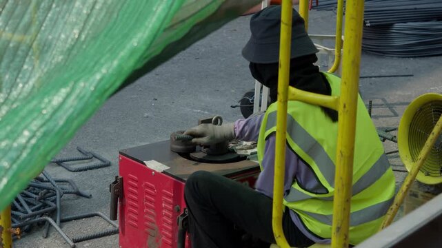 Construction footage shows worker bending reinforcement bars while sitting low beside machine, with surrounding debris and unprotected metal creating constant hazard.