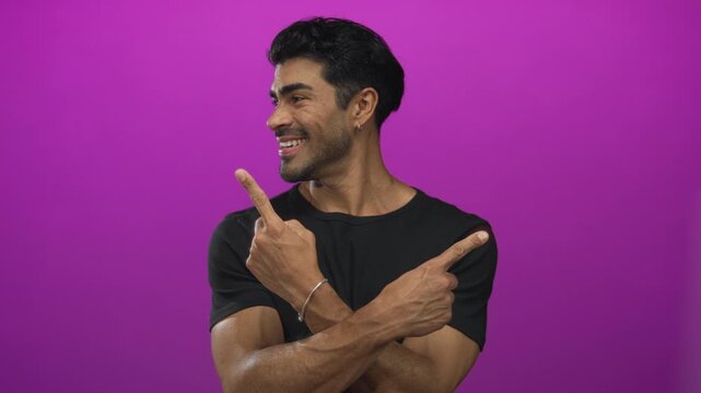 Smiling hispanic man crossing arms and pointing index fingers in purple studio setting; choice decision confidence.