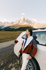 Fototapeta premium Woman and car in mountains on travel roadtrip, portrait in nature with outdoor adventure vibe, leaning by suv on dirtroad, scenic landscape and relaxed exploration journey.