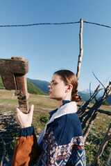 Obraz premium Woman portrait in countryside by a wooden fence, wearing patterned sweater in profile against mountains. Rural outdoors scene with sky, grass and serene seasonal mood.