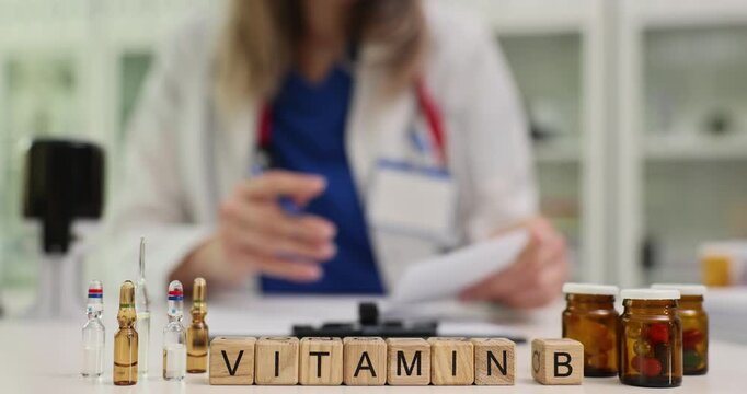 Woman physician writes prescription for vitamins sitting at desk. Wooden blocks form term Vitamin B near containers filled with tablets for patient