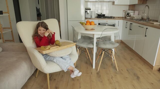 Happy Girl Eating Pear in a Comfortable Chair in Her Modern Home