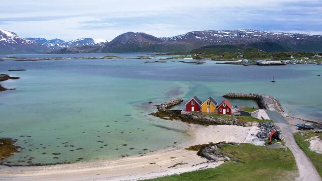 Aerial of small traditional rorbu fishing huts with snow covered mountain background on summer Sommaroy island Norway