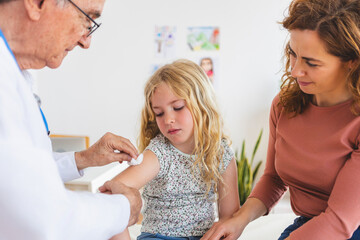 Obraz premium Senior male doctor making vaccination to little girl at hospital room. Children healthcare concept.