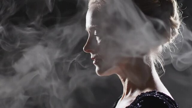 A captivating side profile of a woman is bathed in soft, dramatic light, as graceful tendrils of white smoke or vapor gently swirl around her face and delicate features against a dark, enigmatic backg