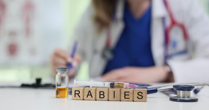 Word Rabies on wooden blocks near vaccine and stethoscope on doctor desk. Female physician plans dangerous viral disease treatment in hospital