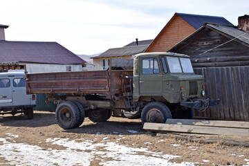 Fototapeta premium Rural scene in Khuzhir, Olkhon Island, with old Soviet truck parked among wooden houses in a quiet Siberian settlement.