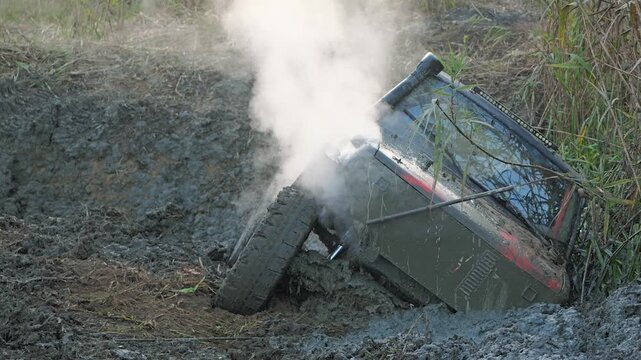 An off-road vehicle got stuck sideways in a deep mud hole during an extreme off-road competition. Steam billows from the overheating engine. Front view