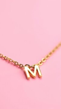 Macro Close-Up of Gold Letter M Initial Pendant Necklace on Pink Background