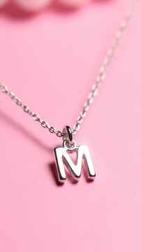 Silver Initial Letter M Pendant Necklace Hanging Against Pink Background