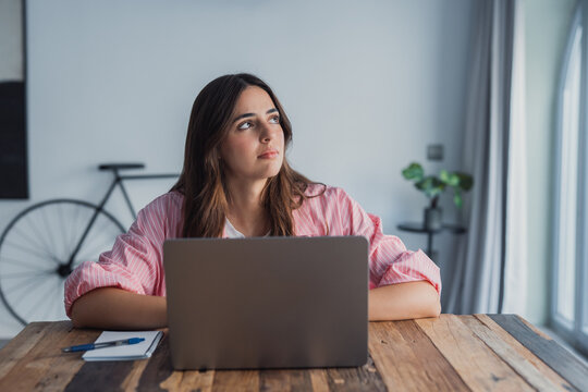 A frustrated and stressed woman sits at her desk near a laptop, holding her head in despair after receiving bad news by email, dealing with dismissal fears, financial problems, personal stress