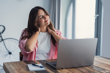 Obraz premium Tired woman feels neck pain, rubs tensed muscles seated at table, suffers from chronic shoulder back ache after long laptop usage, sedentary work, poor posture, health problems, fibromyalgia concept