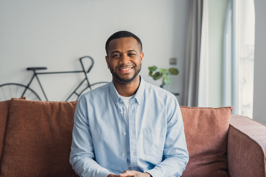 Head shot close up smiling handsome young african ethnicity biracial cheerful man looking at camera, having fun enjoying video call conversation with friends, resting on comfortable sofa at home.&nbsp;