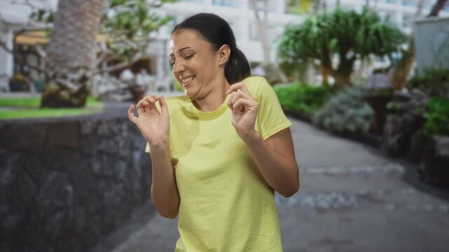 Young hispanic woman with hands raised recoiling on a street walkway wearing a yellow t shirt; disgust aversion.