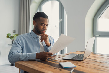 A concentrated African American manager sits at his desk reading a letter and analyzing company...