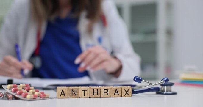 Word Anthrax on wooden cubes near pills blister and stethoscope in hospital. Female doctor works with medical records as sits at workplace