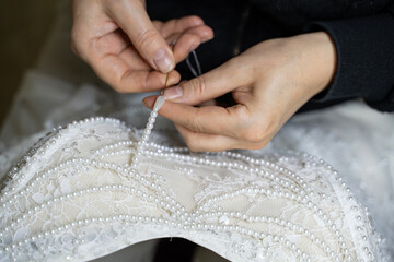 Obraz premium Designer is sewing pearls onto wedding dress (stock photo)