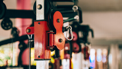 Detailed view of red gym pulley system in fitness equipment, useful for strength training and workout machine parts visuals.
