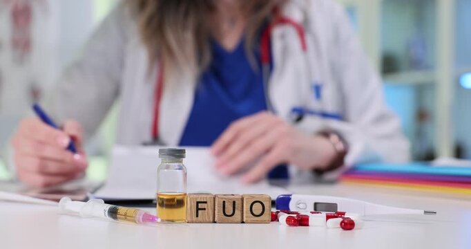FUO abbreviation on wooden blocks near digital thermometer by syringe and drugs in hospital. Female doctor analyzes patient test results in clinic