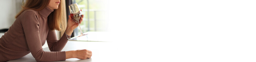Young woman with glass of red wine in hand. Unrecognizable person with glass, alcohol. Banner. Girl holding glass standing near table in kitchen, white space on side for text