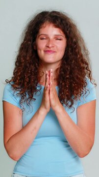 Young woman slyly rubbing hands together, expressing scheming, cunning, mischievous and playful intentions. Girl on gray background demonstrates secretive, sneaky gesture with humorous, tricky emotion