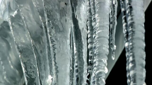 Closeup of melting icicles dripping from house gutters, forming an ice dam after a winter freeze, highlighting cold weather damage and home maintenance risks.