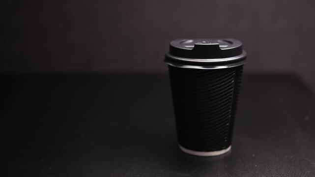 Minimalist black disposable coffee cup with lid on a dark surface, studio lighting